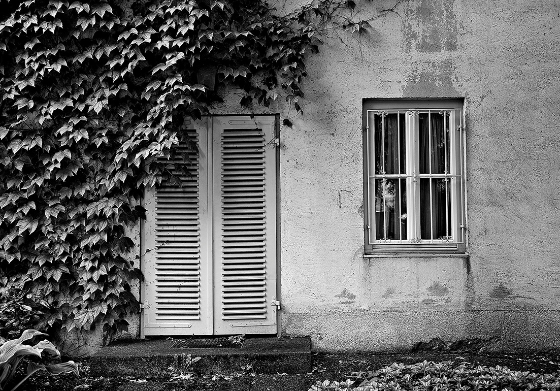 mit Schlagladen verschlossene Tür zum Garten und vergittertes Fenster an einem Wohnhaus