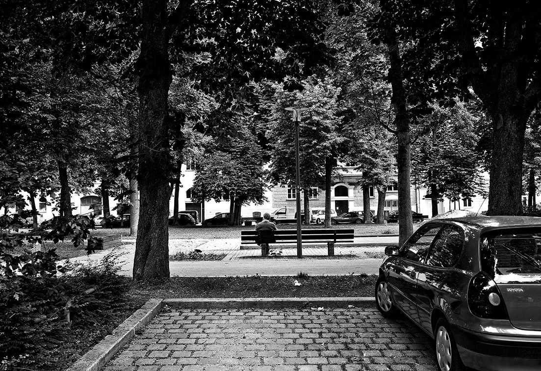 parkendes Auto, Mann auf einer Parkbank im Westend, München, Bayern, Deutschland